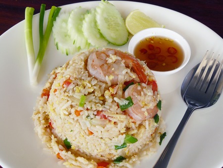 Delicious  fried rice. Shrimp fried rice with cucumber, onion and Thai's fish sauce spicy in a clean white plate on wooden backgroundの写真素材