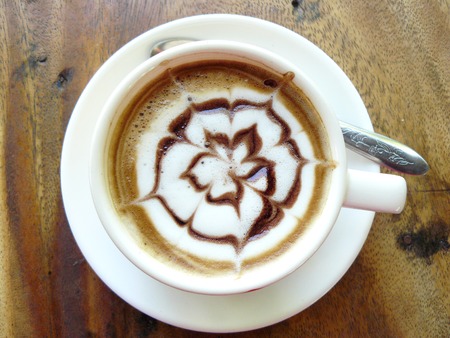 Hot cup of coffee cappuccino decorated chocolate flower in white creamy on wooden tableの写真素材