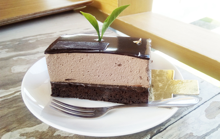 Delicious sweet Brownie Chocolate Cream Cake decorated with green tea leaves in a white plate on wooden background.の写真素材