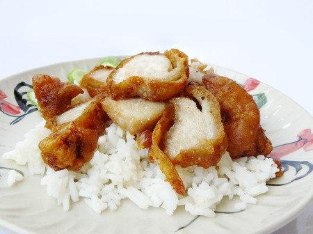 Close up the delicious crispy fried sliced pork served with rice and cucumber in Thai primitive plate isolated on white background.の写真素材