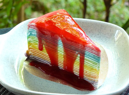 Colorful layer of rainbow crepe cake poured topping strawberry jam, bakery in modern plate.の写真素材