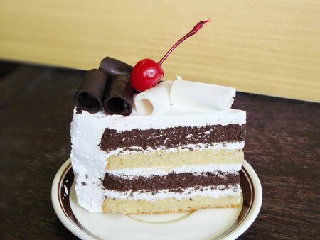 Delicious black and white chocolate cake decorated with red cherry on wooden backgroundの写真素材