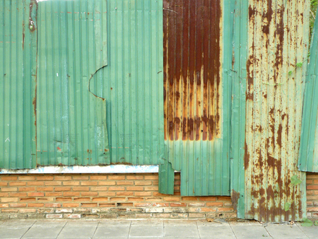 Old green and rusty zinc wall seam continue on red bricks fence for background and texture.の写真素材