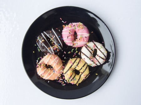 Close up top view of Mini donuts with colorful sugar topping on a black plate isolated on white background.の写真素材