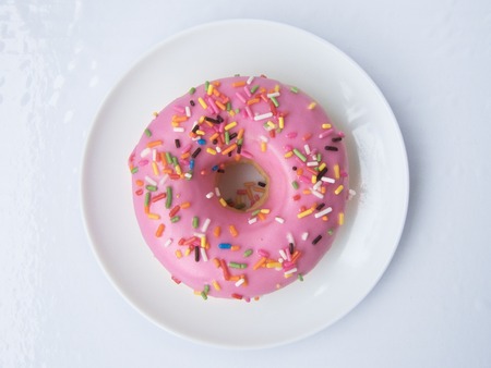 Close up top view of Pink Strawberry Donut decorated with colorful sugar topping on a white plate isolated on white background.の写真素材