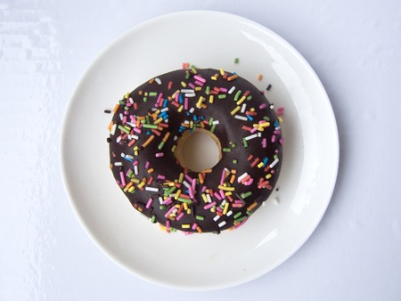 Close up top view of Chocolate Donut decorated with colorful sugar topping on a white plate isolated on white background.の写真素材
