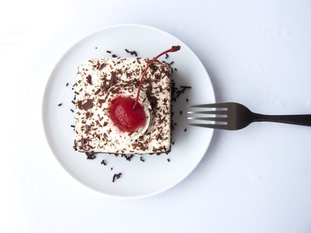 Close up top view of mini Coffee black forest cake, Delicious the chocolate - rum cake decorated with coffee milk cream and red cherry on a white plate and fork isolated on white background.の写真素材