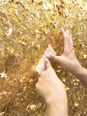 Close up hands of buddhist putting gold leaves on sculpture surface of big buddha, The gold leaves texture in the sunlight.の写真素材