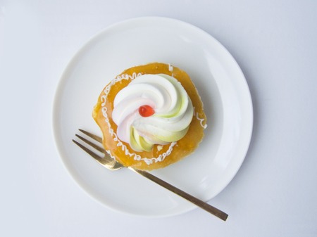 Close up the top view of orange vanilla cream cake. Small size of vanilla cake decorated with orange jam and cream on the top of cake. Putting on white plate and fork, Isolated on white background.の写真素材