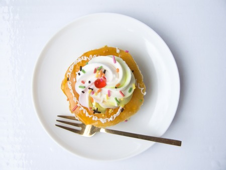 Close up the top view of orange vanilla cream cake. The vanilla cake decorated with orange jam, cream, color sugar on the top of cake. Putting on white plate with fork, Isolated on white background.の写真素材