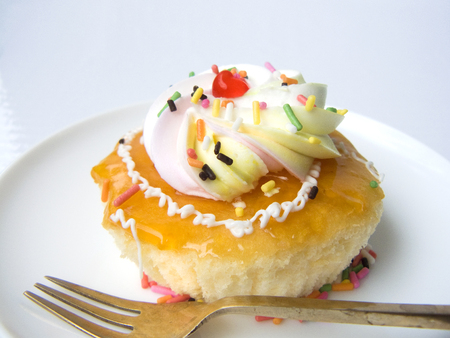 Close up the top view of orange vanilla cream cake. The vanilla cake decorated with orange jam, cream, color sugar on the top of cake. Putting on white plate with fork, Isolated on white background.の写真素材
