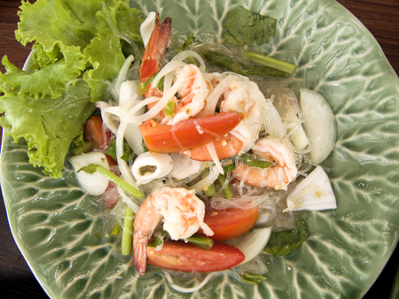 Delicious Asian food. Close up of Thai spicy and sour seafood salad on a plate on wooden table background.の写真素材