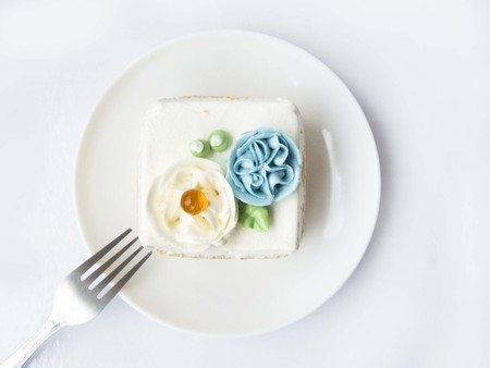 Close up top view of Chiffon snow flower cake. The chiffon vanilla cake decorated with cream of flower and orange jelly ball. Putting on white plate and fork. Isolated on white background.の写真素材