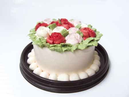 Close up side view of colorful sweet milky vanilla cake decorated with cream vanilla in rose garden pattern on a brown plate isolated on white background.の写真素材