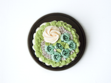 Close up top view of colorful sweet milky vanilla cake decorated with cream vanilla in green rose garden pattern on a brown plate isolated on white background.の写真素材