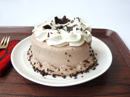 Close up front view of Chocolate Cookie Cream Cake; Delicious chocolate cake decorated with choco cookie on a white plate and wooden tray isolated on white background.の写真素材