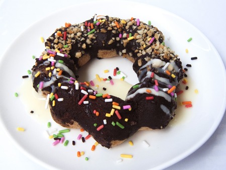 Close up top view of Chocolate Donut decorated with colorful sugar topping on a white plate isolated on white background.の写真素材