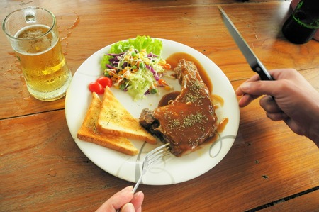 Eating pork steak with black pepper sauce and drinking a beer. Delicious dinner favorite food on a white plate on classic wooden table background.の写真素材