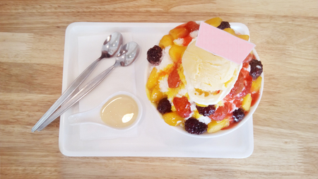 Delicious Asia-Asian eating food, Bing su: Korean shaved milk ice dessert with sweet toppings, various mix fruit, strawberry jam and vanilla ice-cream. Close up top view on wooden table background.の写真素材