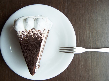 Delicious Chiffon - chocolate cake, The chocolate - chiffon cake decorated with milk cream and chocolate topping on a white plate with fork. Close up top view on wooden table background.の写真素材