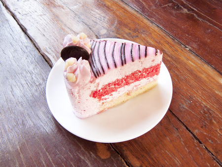 Delicious strawberry white chocolate cake, The layer strawberry cake decorated with cream chocolate and pink chocolate on a white plate. Close up side view on wooden table background.の写真素材