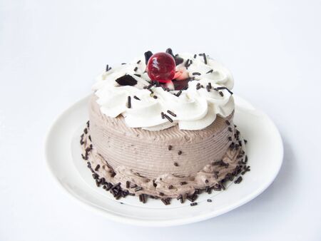 Delicious Chocolate Cream Cake. Close up front view of a chocolate cake decorated with chocolate chip, white cream, dark sugar color and jelly ball on a white plate. Isolated on white background.の写真素材