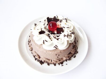 Delicious Chocolate Cream Cake. Close up front view of a chocolate cake decorated with chocolate chip, white cream, dark sugar color and jelly ball on a white plate. Isolated on white background.の写真素材