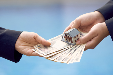 Two businessmen conduct a house sale with a model house and Yen banknotes valued at 10000 yen.using as background business concept and real estate concept with copy space for your text or design.の写真素材