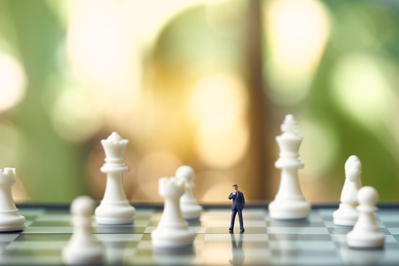 Miniature businessmen standing on a chessboard with a chess piece on the back. as background business concept with copy space.の写真素材