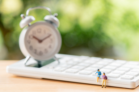 Miniature 2 people sitting on white calculator using as background business concept and teamwork...