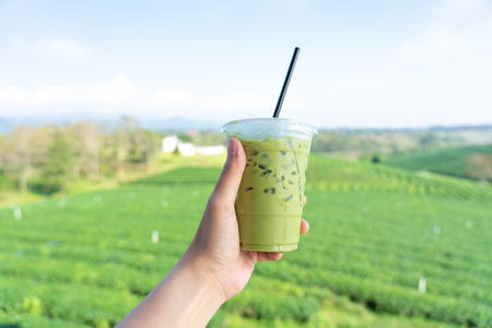 Young man hand holding a glass of green tea drink Filed with a large tea plantation background Green tea is a healthy drink Useful to the bodyの写真素材