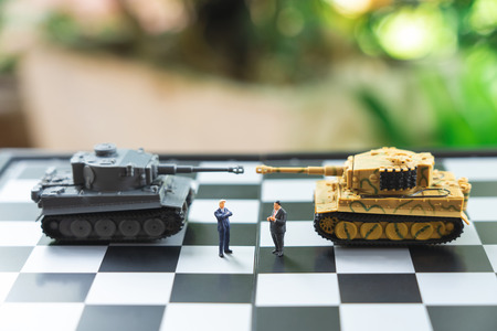 Miniature people businessmen standing on a chessboard with a Tank model on the back Negotiating in business. as background revolution concept and strategy concept with copy space.の写真素材