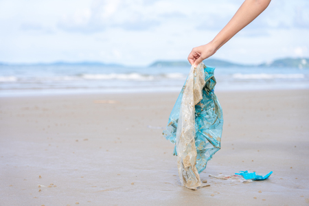 Womanâs hand picking up used plastic bag on sand beach, cleaning seaside beach.  Environmental pollution, Ecological problem and  Marine pollution concept.の写真素材