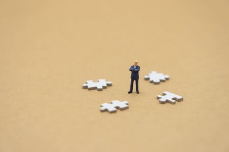 Miniature people businessmen standing on white Jigsaw. The concept used in selecting personnel to...