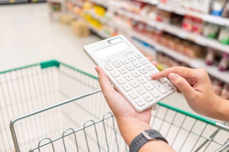 A beautiful Asian woman holding a calculator to calculate the cost and price reduction in a supermarket. Concept of price reduction, saving and valueの写真素材