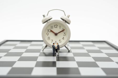 Miniature 2 people businessmen Shake hands standing on a chessboard with a chess piece on the back Negotiating in business. as background business concept and strategy concept with copy space.の写真素材