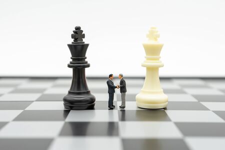 Miniature 2 people businessmen Shake hands standing on a chessboard with a chess piece on the back Negotiating in business. as background business concept and strategy concept with copy space.の写真素材