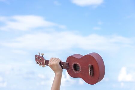 The hand of the girl holding the guitar in the background is a bright sky, giving a feeling of...