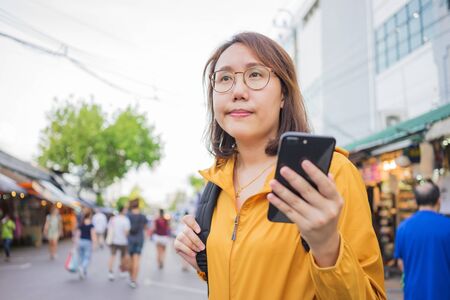 Portrait Beautiful Asian women stand to hold smartphones in the Chatuchak market in Thailand. Bangkok is a tourist attraction for foreigners.の写真素材
