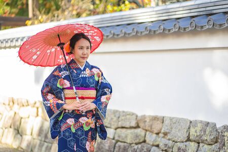 Geishas girl wearing Japanese kimono among red wooden Tori Gate at Fushimi Inari Shrine in Kyoto, Kimono is a Japanese traditional garment. The word "kimono", which actually means a "thing to wear"の写真素材