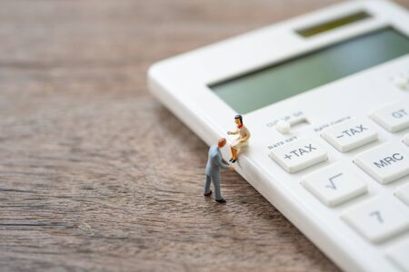 Miniature people sitting on white calculator using as background business concept and teamwork concept with copy space and white space.の写真素材