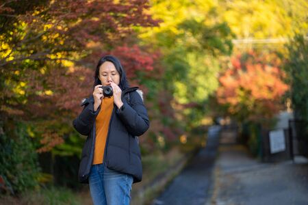 Young beautiful photographer with the professional camera taking photo beautiful autumn colourful maple leaf in Kyoto Japan.の写真素材
