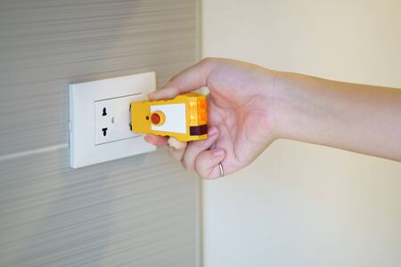 Hand holding electric tester for checking plug at the power outlet in on the wall. Check the quality...
