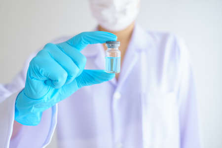 Female doctor or scientist in laboratory with stethoscope holding holds an injection syringe and...