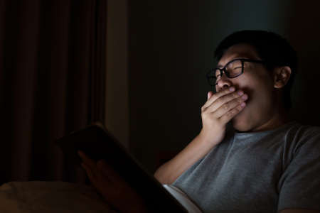 An Asian man between the ages of 35 and 40 plays a laptop in his bed. Concept of technology, poor health, insufficient restの写真素材