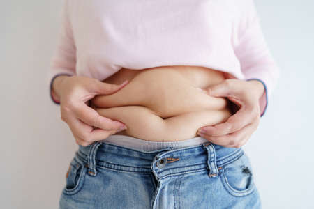 Women body fat belly. Obese woman hand holding excessive belly fat. diet lifestyle concept to reduce belly and shape up healthy stomach muscle.の写真素材