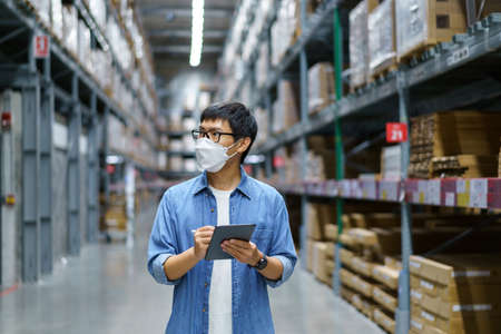 New Normal Asian men, staff, product wearing face mask. counting Warehouse Control Manager Standing, counting and inspecting products in the warehouseの写真素材