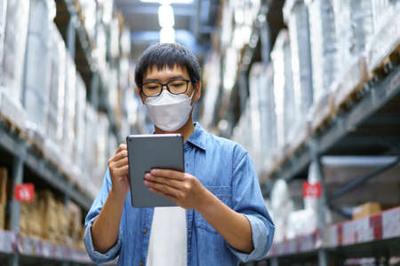 New Normal Asian men, staff, product wearing face mask. counting Warehouse Control Manager Standing, counting and inspecting products in the warehouseの写真素材
