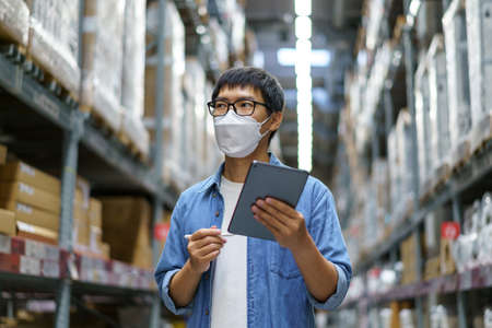 New Normal Asian men, staff, product wearing face mask. counting Warehouse Control Manager Standing, counting and inspecting products in the warehouseの写真素材