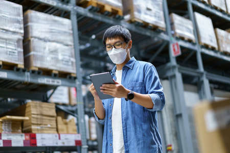 New Normal Asian men, staff, product wearing face mask. counting Warehouse Control Manager Standing, counting and inspecting products in the warehouseの写真素材